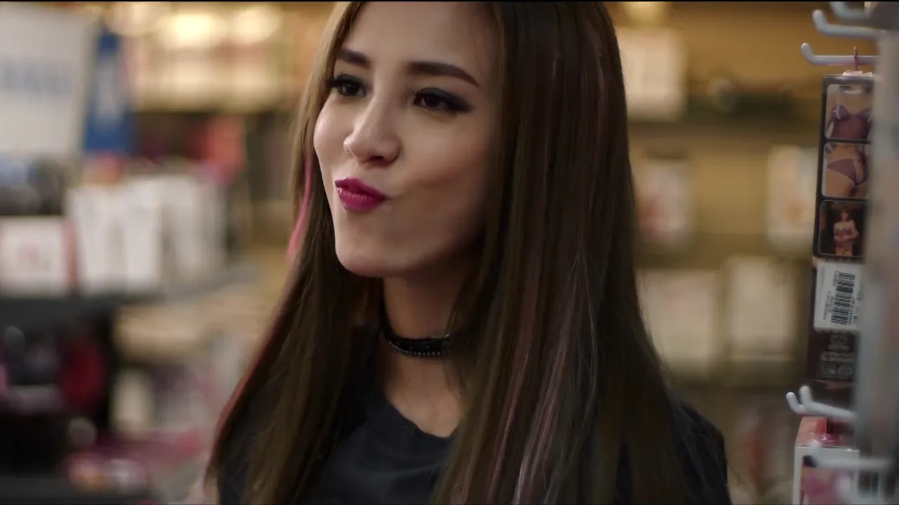 Close-up of a long-haired woman with pink lipstick beside a convenience-store display